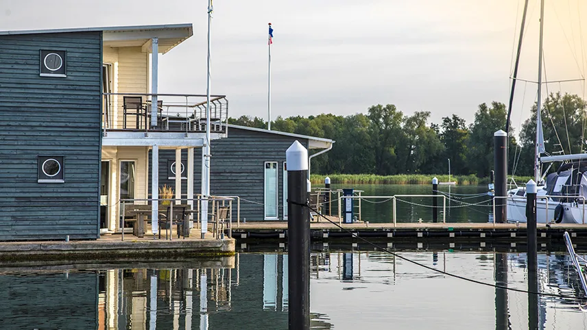 Ett av de flytande semesterhusen i hamnen. Ett trähus i två våningar med runda fönster och en brygga med båtar alldeles utanför.