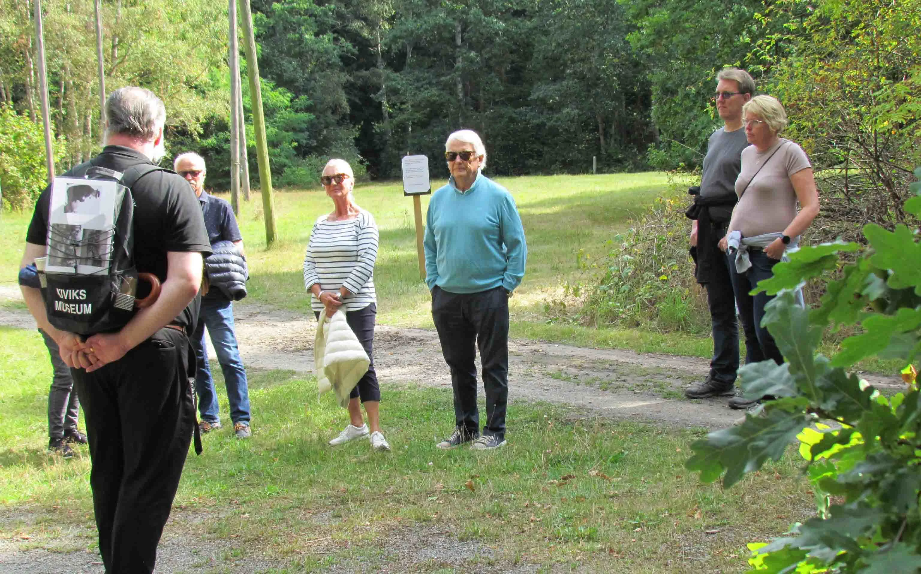 Vandring på Kivik hvor en gruppe mennesker lytter til guide i grønne omgivelser.