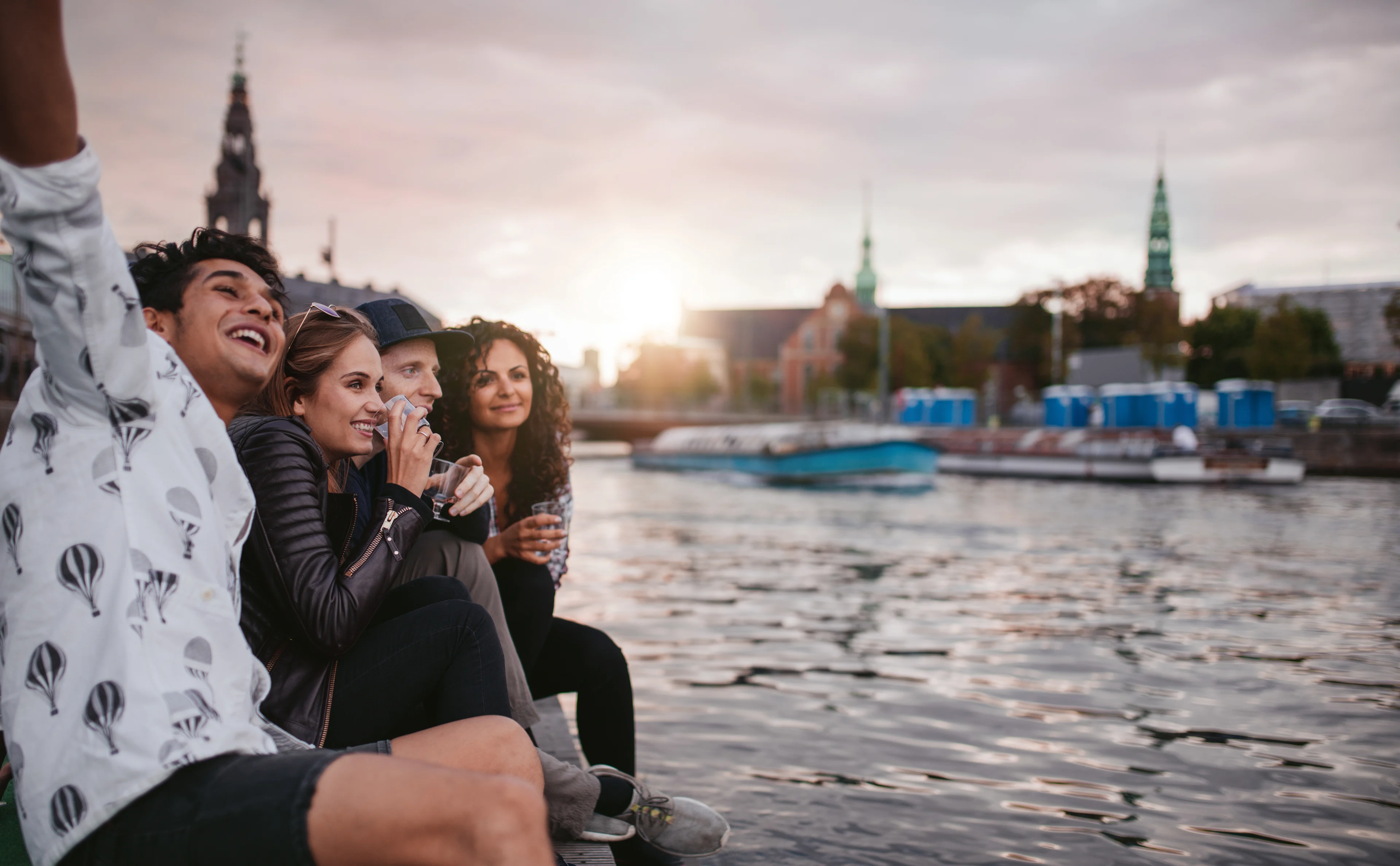 Fyra personer sitter vid vattnet i Köpenhamns hamn och tittar ut över staden.