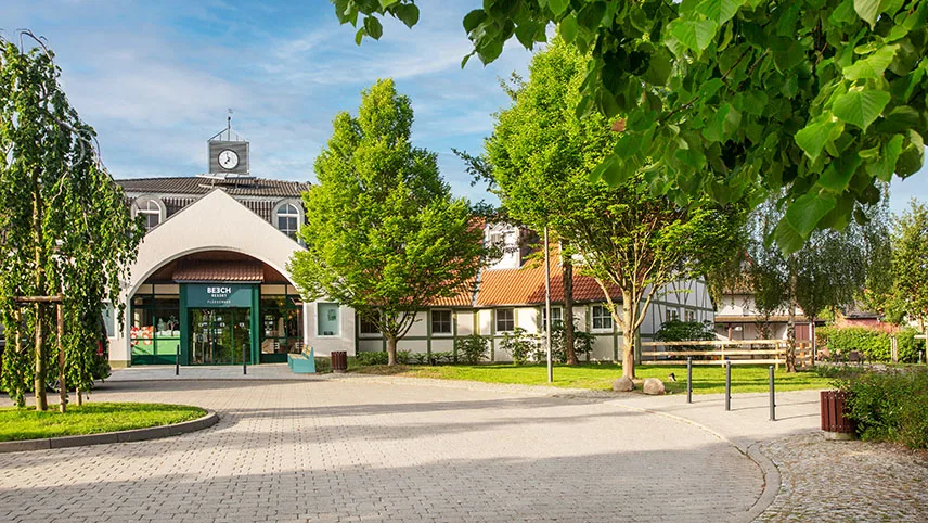 Ingången till BEECH Resort Fleesensee, omgiven av grönskande träd och frodiga gräsmattor.