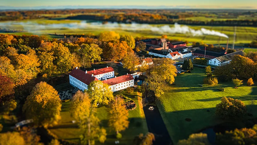 Kragerup Gods sett från luften på hösten, med träd i höstprakt, vidsträckta fält och dimma på åkrarna.