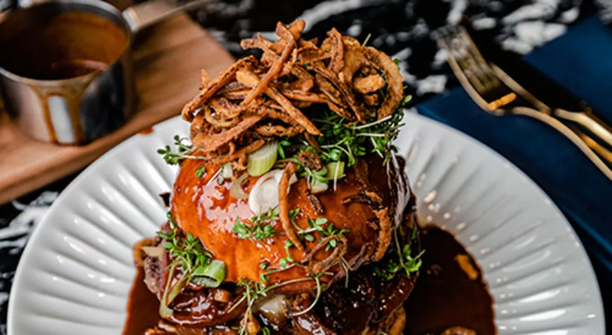 Närbild av restaurangens berömda biffburgare med briochebröd, lökringar och sås.