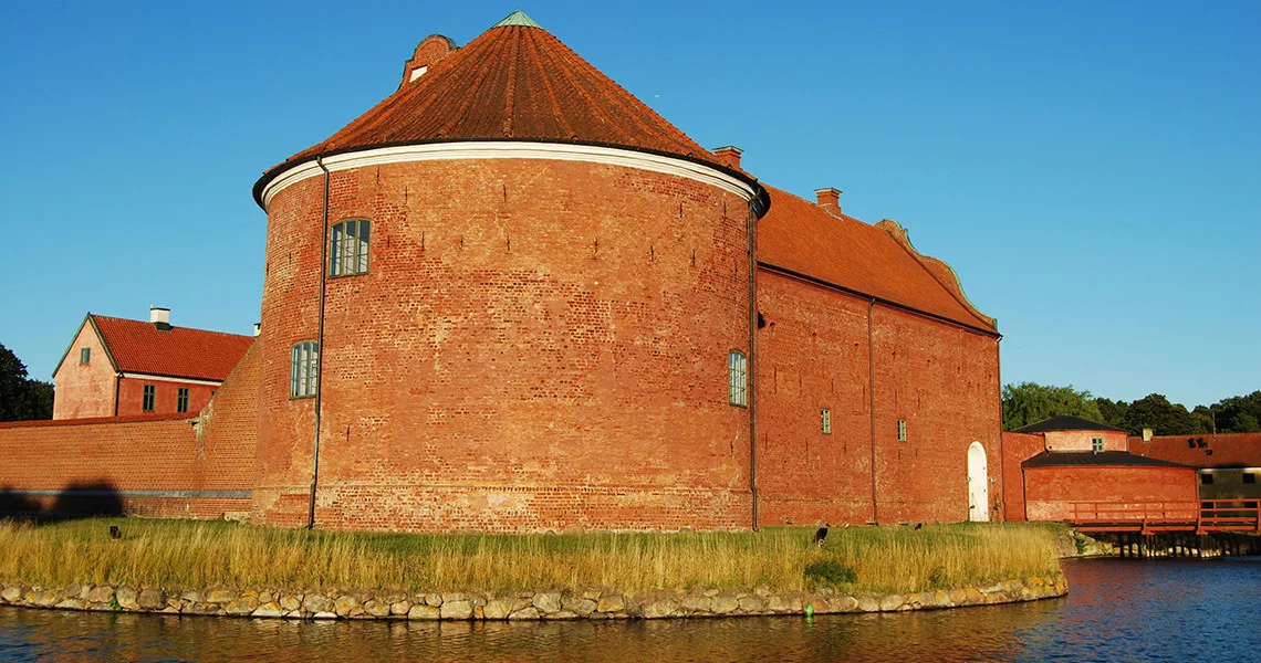 Stort rundt tårn med forbindende bygninger og vand på to sider.