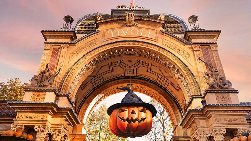 Ingången till Tivoli mot en ljusrosa himmel. Längst uppe i valvet hänger en stor pumpa med häxhatt på.