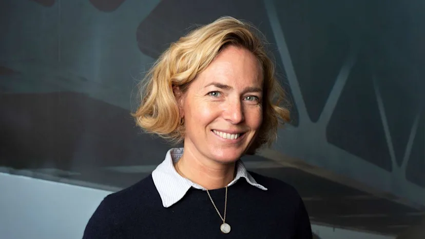 På billedet ser man Jeannete Birkholm, Anlægsdirektør hos Øresundsbroen, stå udenfor foran en moderne bygning med lys stenfacade og store glaspartier. Baggrunden viser efterårsfarver med grønne og gule træer og blødt naturligt lys, der skaber en professionel stemning.