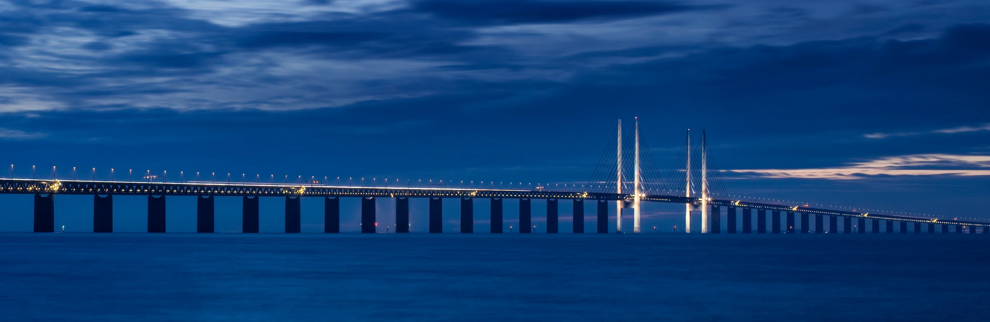 Øresundsbron med standardbelysning på en mørkeblå himmel og mørkeblåt hav.