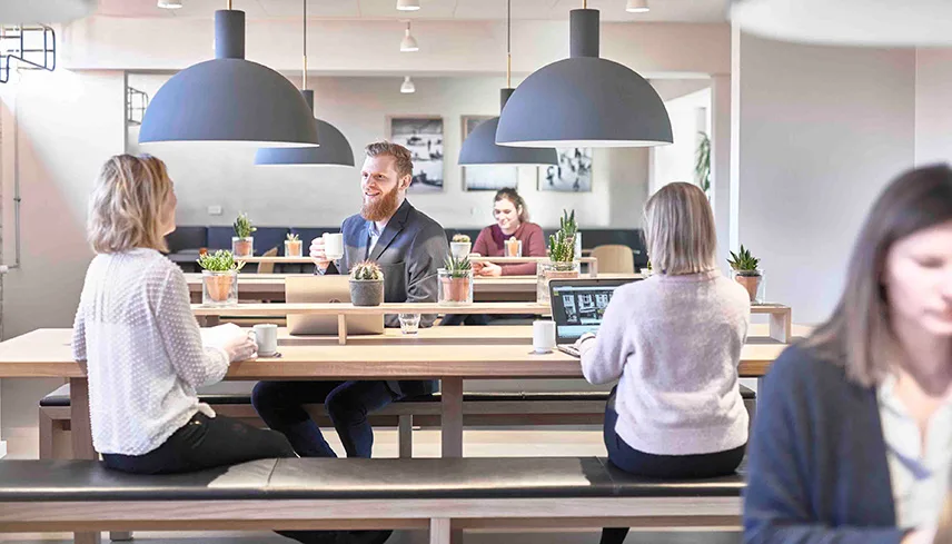 Bild från matsalen med långa bord och bänkar och gäster som sitter och pratar, jobbar vid sina datorer och dricker kaffe.
