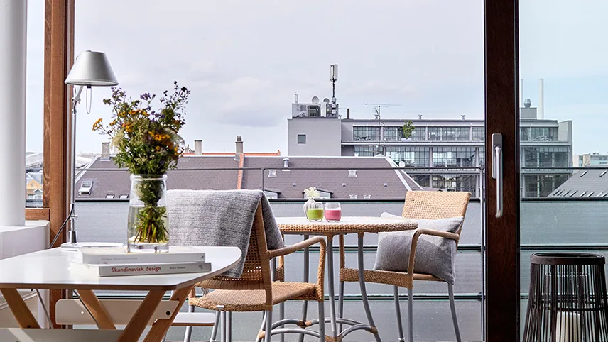 Utsikt från en av hotellets lägenheter. Man ser elegant inredning med ett bord med blommor i en vas och en altan med utemöbler.