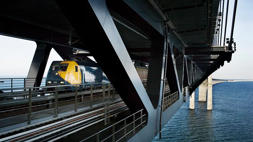 Tog suser forbi på jernbaneskinnerne under Øresundsbroen