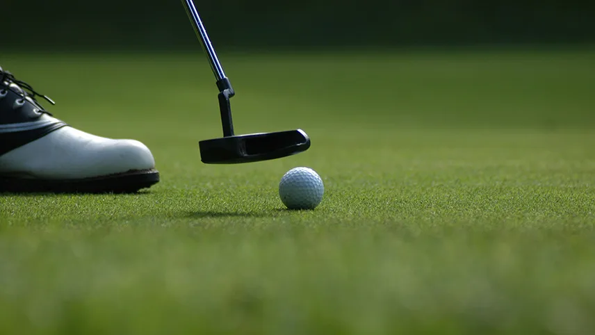 En golfspelare på en grön golfbana. I bild syns spetsen av en vit golfsko, en golfklubba samt en boll.