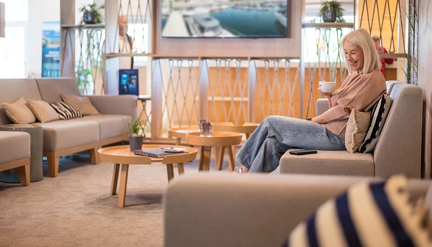 Hotellets lobby med ljusa möbler och sittgrupper i dämpade färger. En gäster sitter i en av sofforna och dricker en kopp kaffe.