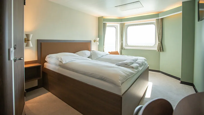 En Commore-hytt på fartyget. I mitten syns en dubbelsäng med sänggavel och vägglampor. Den ena väggen är målad i ljusgrönt.