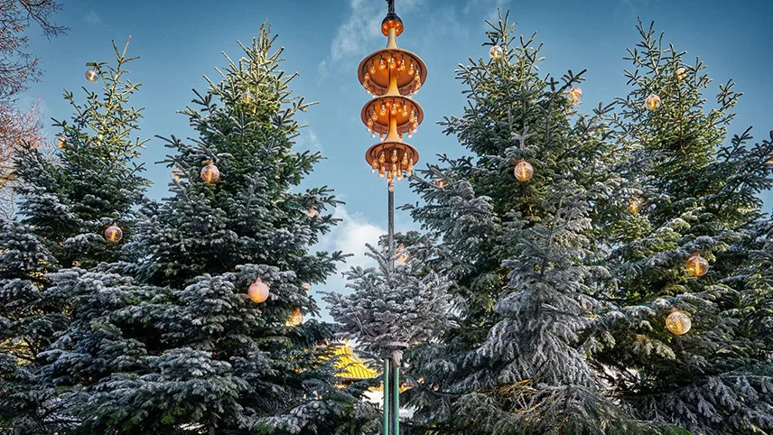 Snötyngda julgranar med julkulor och pynt mot blå vinterhimmel.