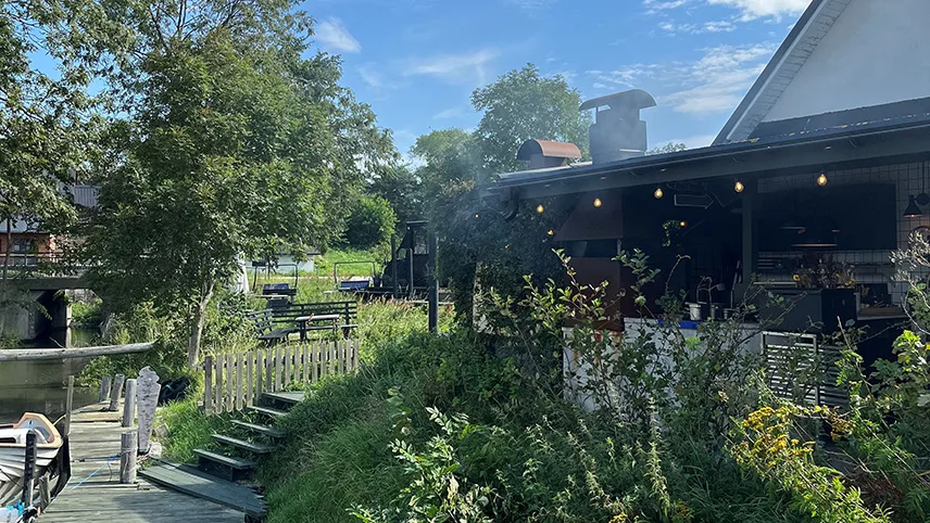 Terrassen på Hörte Brygga med grømme områder, lyskæder og røg fra en grill.