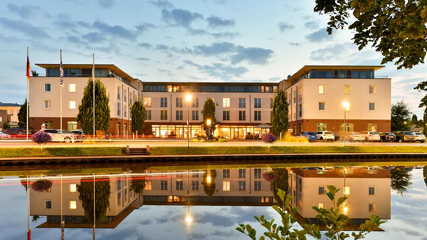 Hotellfasad på kvällen, reflekterad i en stilla kanal framför byggnaden