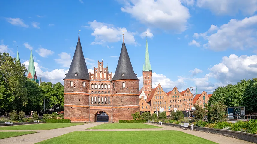 Den gamla stadsporten i Lübeck, mot blå himmel och grönskande träd.