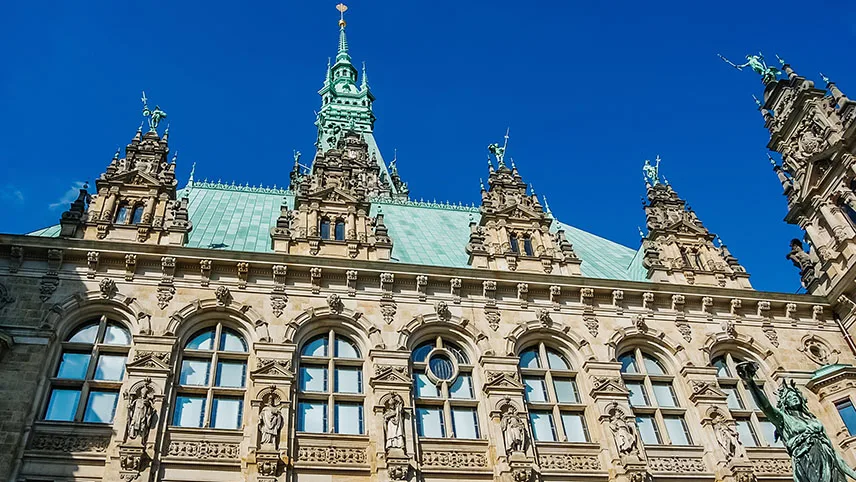 Rådhuset i Hamburg med koppartak, högt torn och sirligt dekorerad fasad mot en klarblå himmel.