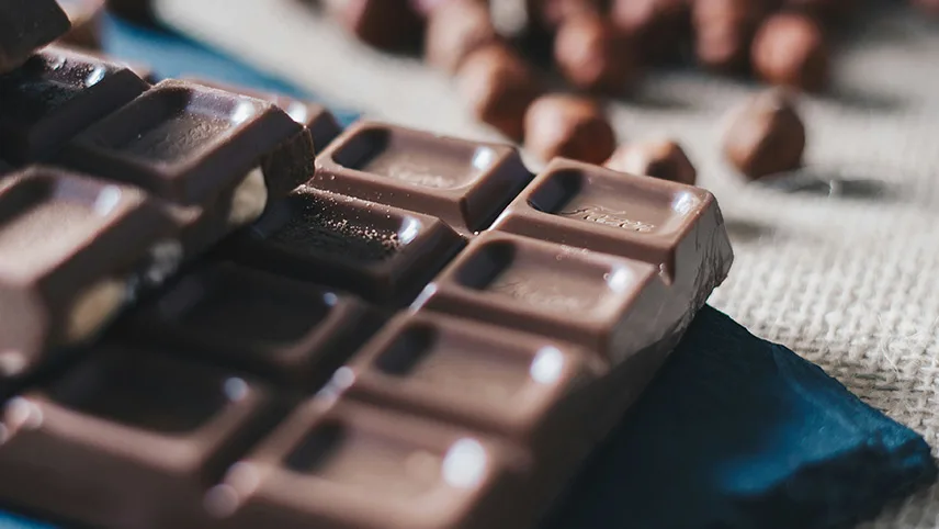 Närbild på kakaobönor och en chokladkaka på en duk i gjuteväv.