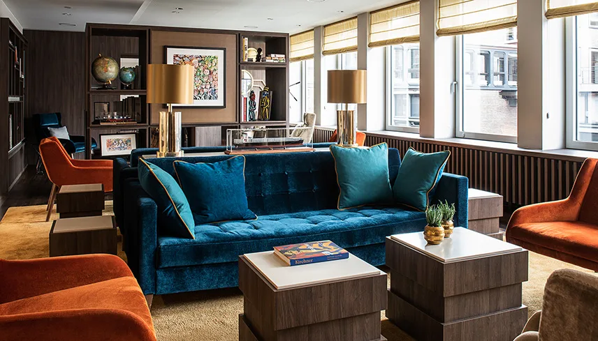 Hotellets lobby med stora fönster, mörka träslag och soffor och stolar i starka färger.