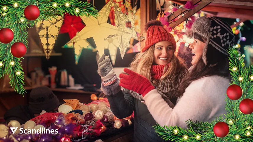 Två kvinnor står på en julmarknad och tittar på julstjärnor som hänger inne i en bod. Kvinnorna är klädda i varma kläder och skrattar.