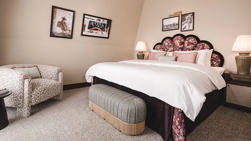 Ett av rummen på Rox Resorts med ljusa väggar, ljus matta och en stor dubbelsäng med snäckformad sänggavel och rosa detaljer. I ena hörnet syns en fåtölj och på väggarna hänger inramade bilder.