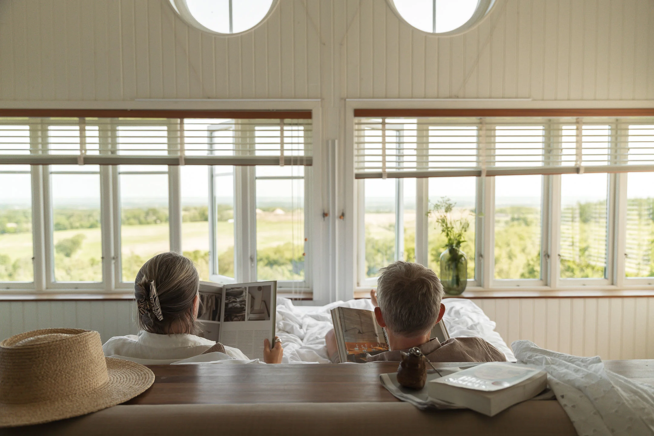 The Lodge terrasse hvor et par ligger i en relaxseng og nyder udsigten over naturen med en bog i hånden.