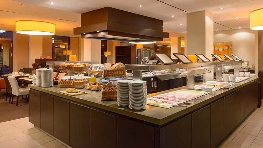 Hotellets frukostmatsal med buffé. På en bänk står tallrikar i travar och diverse bröd, pålägg och annat ligger vackert uppdukat.