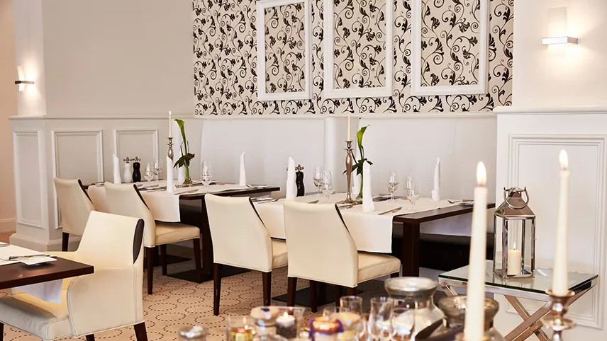 Hotellets ljusa och fräscha restaurang serverar god mat för alla smaker. Här ser man flertalet dukade bord, med tända ljus och blommor.