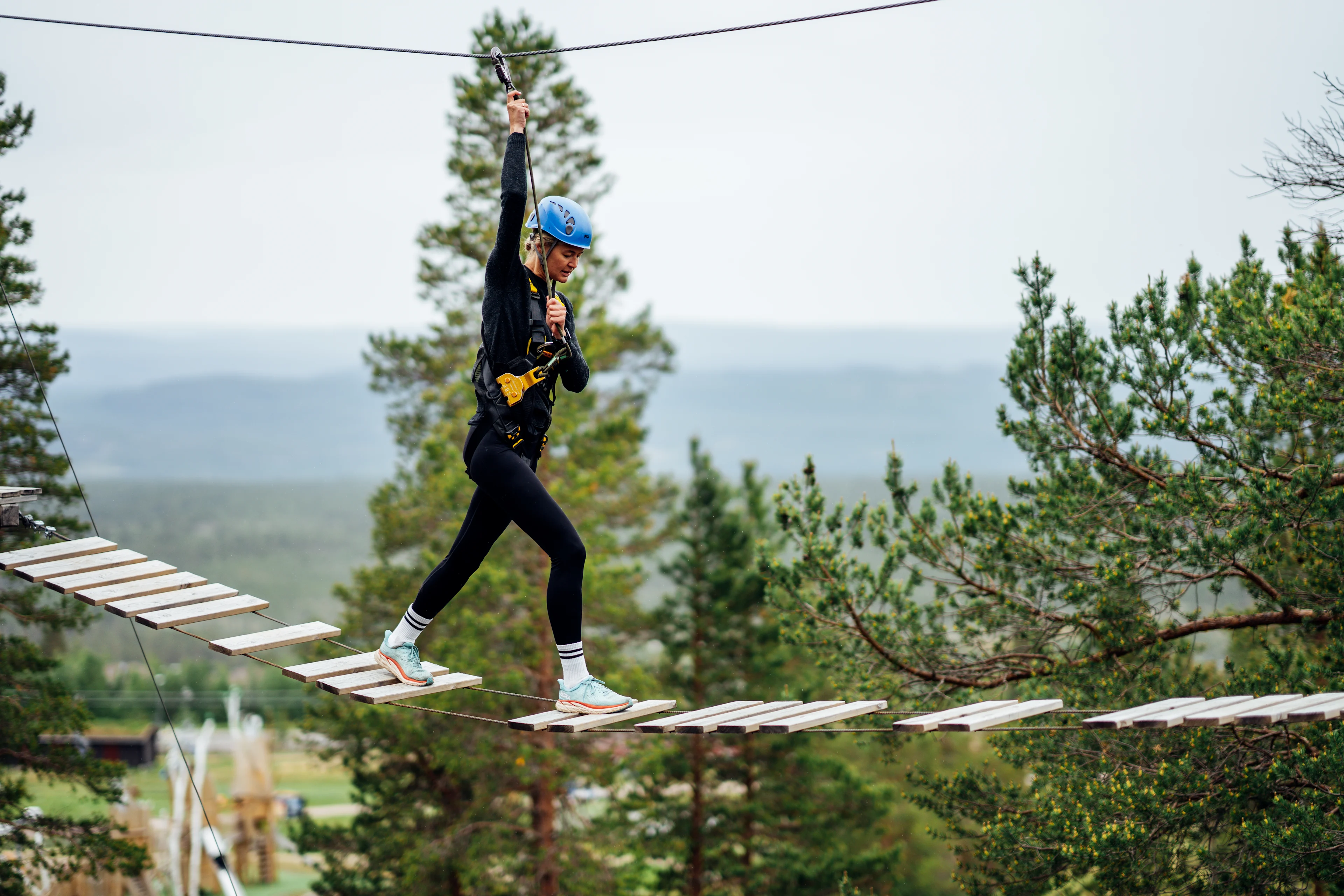 Kvinde går over gangbro iført sele og zipline.