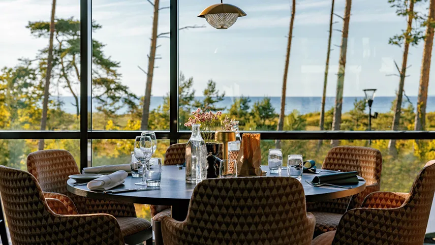 Den nyrenoverede restaurant hos Hotell Riviera Strand med udsigt til natur og strand. Det runde bord er fint dækket med glas og andet.