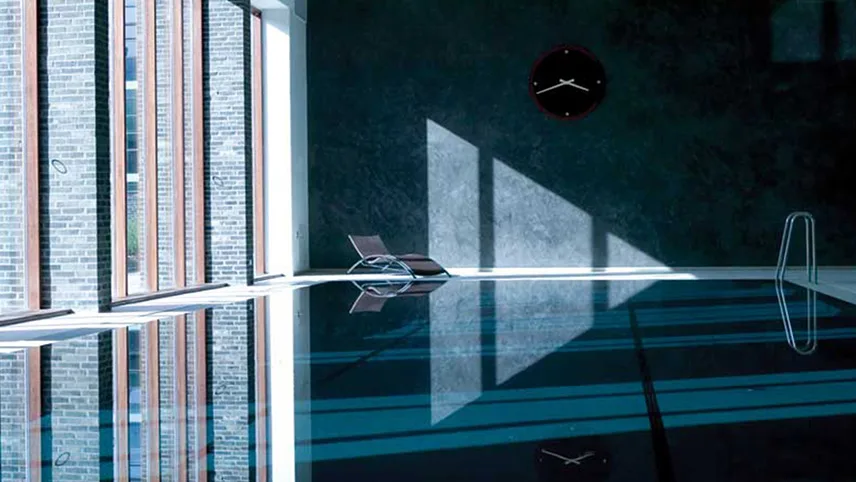 Bild av Charlottenhavens inomhuspool med spegelblankt vatten, stora fönster och en liggstol i ena hörnet.