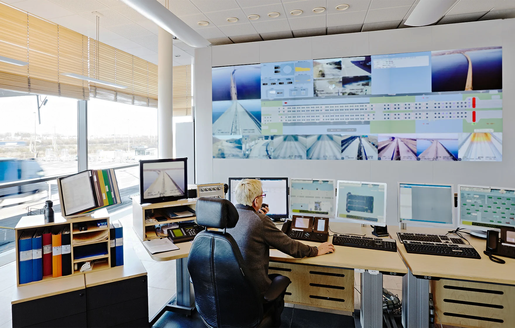 En man på trafikledningscentralen sitter med ryggen mot kameran och tittar på ett stort antal skärmar med övervakningskameror som visar trafiksituationen på Öresundsbron.