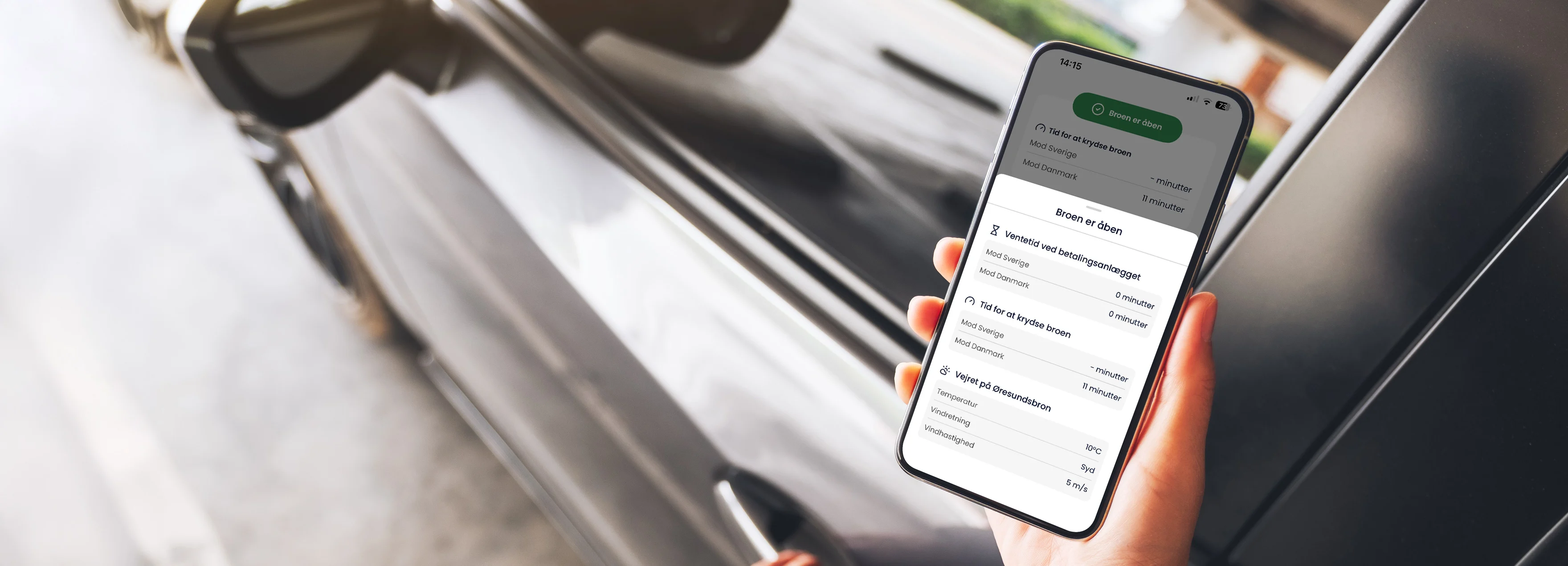Hånd holder iPhone, der viser Øresundsbrons app med en grå bil i baggrunden.