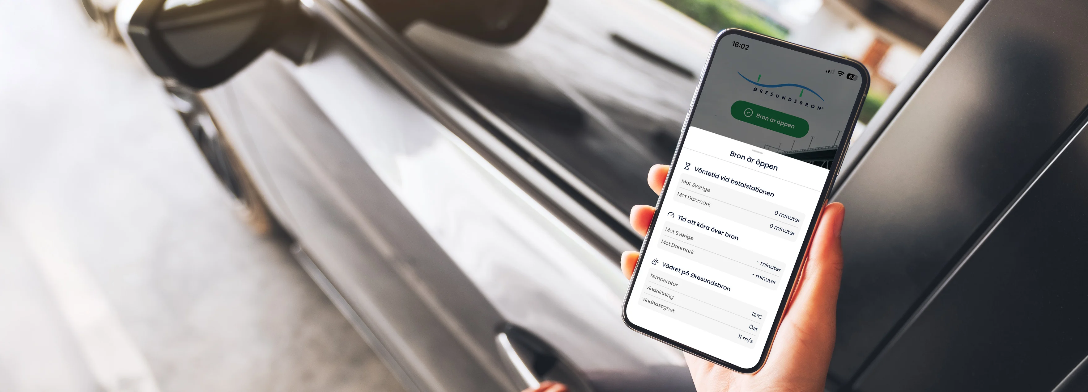Hand håller iPhone som visar Öresundsbrons app med en grå bil i bakgrunden.