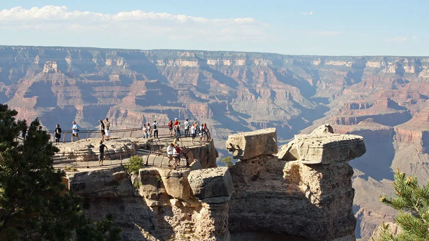 Bild från Grand Canyon med besökare som står uppe på klipporna och tittar ut över landskapet.