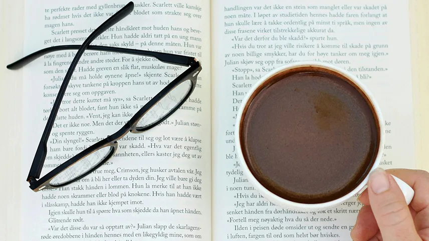 En öppen bok, med kopp kaffe och ett par läsglasögon.