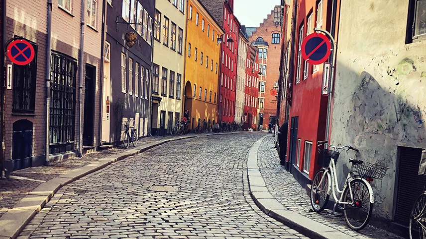 En smal kullerstensbelagd gata med färgglada fasader och smala trottoarer.