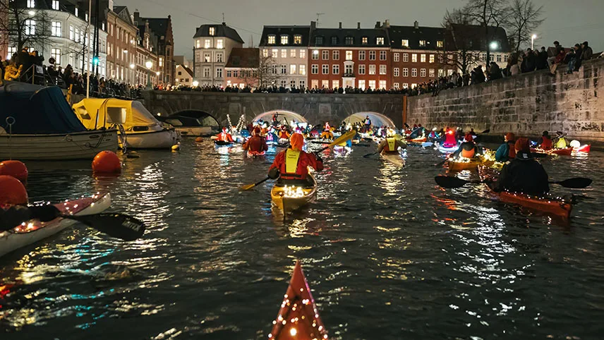 Jultomtar paddlar kajak i en upplyst kanal i Köpenhamn.