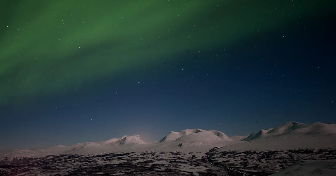 Bjerge dækket af sne og nordlyset, der skinner på himlen.