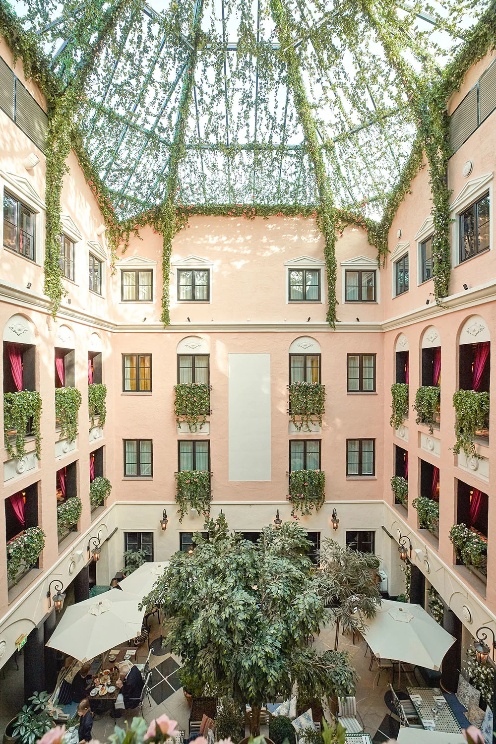Hotel MJs indendørs gård med glasloft, lyserøde vægge og grønne planter.