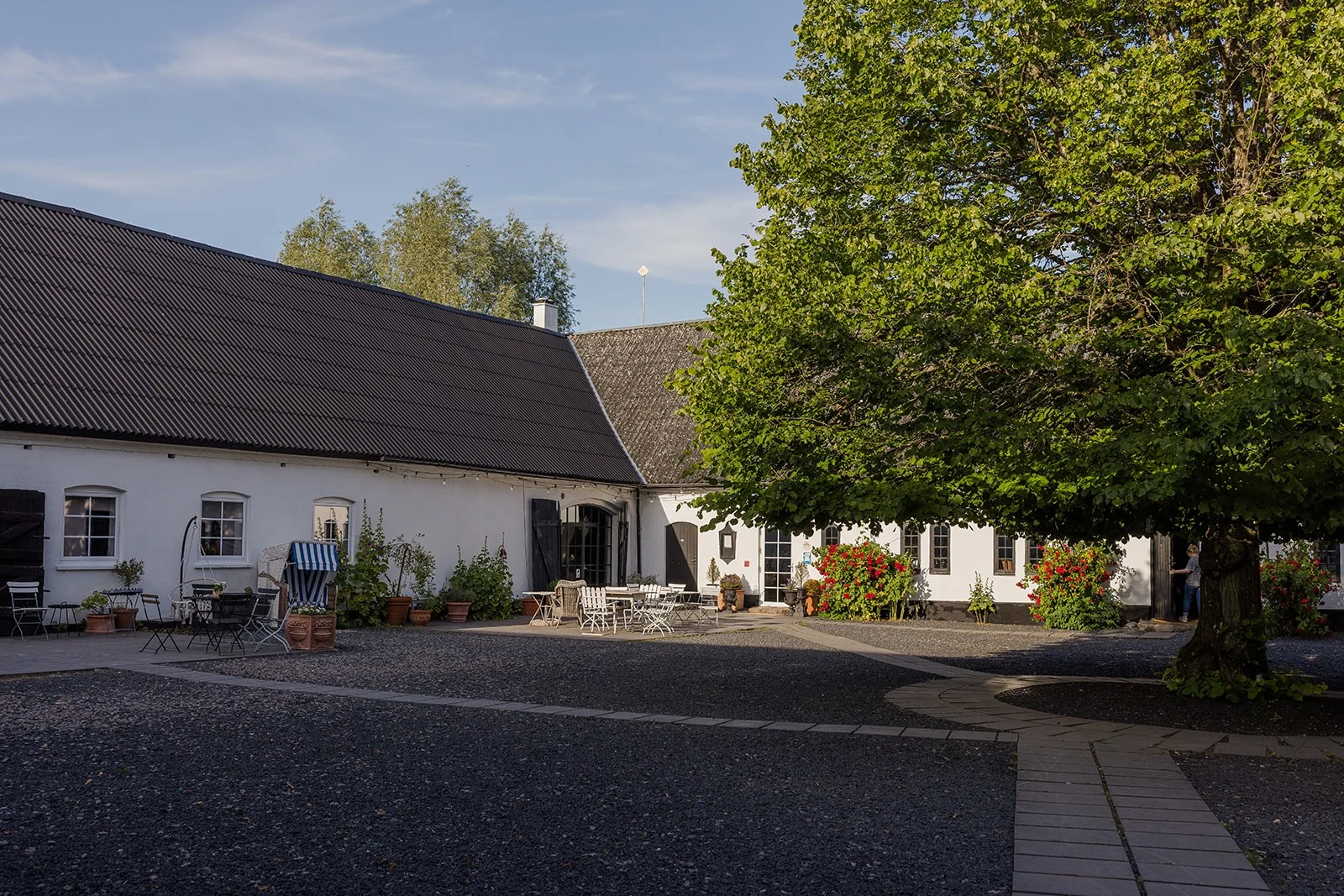 Idala Gård i Sydsverige. Her ses et hvidt stuehus med træer foran og blå himmel.