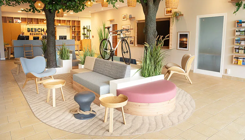 Hotellets lobby med möbler i ljust trä och fräscha färger, träd och växter samt en cykel som står som prydnadssak. I bakgrunden syns receptionsdisken.
