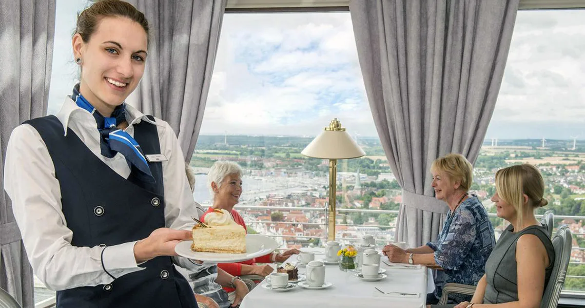 Servitris serverar bakverk till gäster på ett café i Maritim Hotel med utsikt över staden