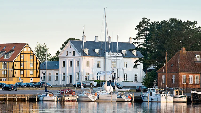 Bandholm Badehotells framsida med båtar och brygga framför.