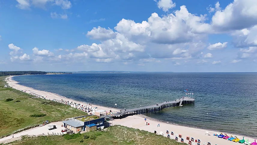 Flygbild över badstranden vid Weissenhäuser Strand. En badbrygga sträcker sig ut i vattnet och på stranden ser man människor som sitter i solen.