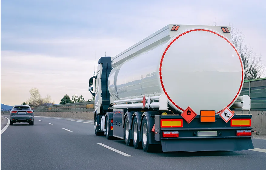 Vit lastbil kör i högerfältet. Röda skyltar längst bak på lastbilen markerar farligt gods.