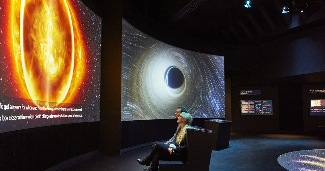 Par som sitter och tittar på stora skärmar på Planetarium i Köpenhamn.