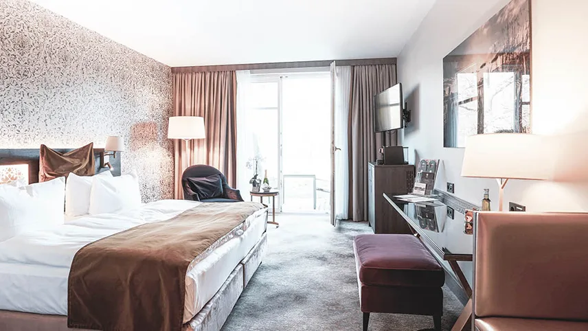 Dubbelrum med bred dubbelsäng bäddad med kritvita lakan, vackra möbler och stora fönster med stort ljusinsläpp.