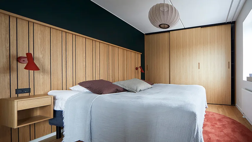 Ett sovrum med vackra träpaneler på väggarna, stor platsbyggd garderob samt en bred dubbelsäng med ljusa sängkläder.