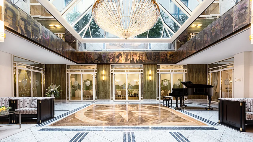 Elegant hotellobby med ett stort glastak, en kristallkrona och ett piano